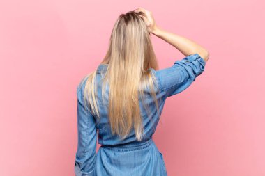 Genç, sarışın, güzel bir kadın bilgisiz ve şaşkın hissediyor, bir çözüm düşünüyor, eli kalçasında, diğeri kafasında, dikiz aynasından.