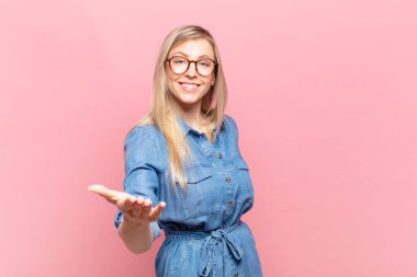 Genç sarışın güzel bir kadın gülümsüyor, mutlu görünüyor, kendinden emin ve arkadaş canlısı, bir anlaşmaya varmak için el sıkışmayı teklif ediyor, işbirliği yapıyor.