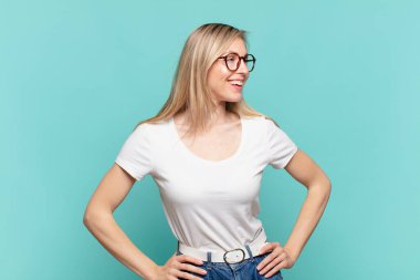 Genç sarışın güzel kadın mutlu, neşeli ve kendinden emin görünüyor gururla gülümsüyor ve iki elini de kalçasında istiyor.