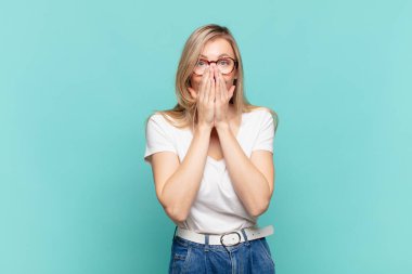 Genç sarışın güzel kadın mutlu, neşeli, şanslı ve şaşkın görünüyor. İki eliyle ağzını kapatıyor.