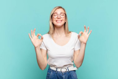 Genç sarışın güzel kadın konsantre olmuş ve meditasyon yapıyor, tatmin olmuş ve rahatlamış hissediyor, düşünüyor ya da bir seçim yapıyor.