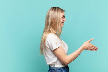 Genç sarışın güzel kadın gülümsüyor, seni selamlıyor ve başarılı bir anlaşma için el sıkışmayı teklif ediyor.