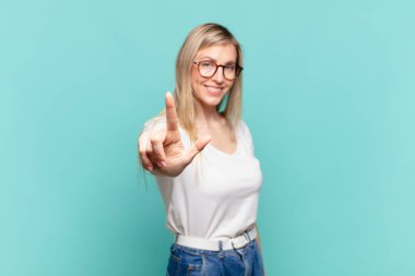 Genç, sarışın, güzel bir kadın gururla gülümsüyor ve gururla bir numaralı pozunu veriyor, kendini lider gibi hissediyor.