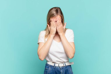 Genç sarışın güzel bir kadın üzgün, hayal kırıklığına uğramış, gergin ve depresif, iki eliyle yüzünü kaplayan, ağlayan