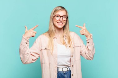 Genç, sarışın, güzel bir kadın, kendine güvenerek gülümsüyor. Geniş bir gülümseme, pozitif, rahat, tatmin olmuş bir tavır sergiliyor.