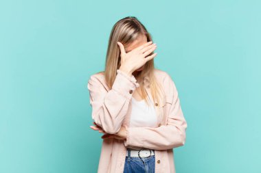Genç sarışın güzel kadın stresli, utanmış ya da üzgün görünüyor, baş ağrısı var, yüzünü eliyle kapatıyor.