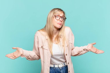 young blond pretty woman feeling clueless and confused, having no idea, absolutely puzzled with a dumb or foolish look