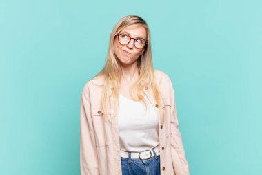 Genç sarışın güzel kadın kafası karışmış ve şaşkın görünüyor, merak ediyor veya bir sorunu çözmeye çalışıyor ya da düşünüyor.