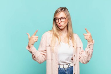 Genç, sarışın, kötü tavırlı, gururlu ve agresif görünen, yukarıyı gösteren ya da elleriyle alay eden güzel bir kadın.