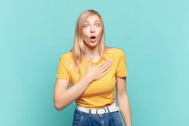 Genç sarışın, güzel bir kadın şok olmuş ve şaşırmış hissediyor, gülümsüyor, el ele tutuşuyor, mutlu ya da şükran duyuyor.