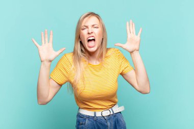 Genç sarışın güzel bir kadın panik ya da öfke içinde bağırıyor, şok olmuş, korkmuş ya da öfkeli, elleri başının yanında.