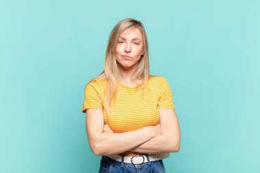 Genç sarışın güzel bir kadın hayal kırıklığına uğramış, hayal kırıklığına uğramış, ciddi görünüyor, kızgın ve kollarını kavuşturmuş.