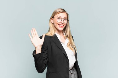 Genç ve güzel iş kadını mutlu ve neşeyle gülümsüyor, el sallıyor, sizi selamlıyor ve selamlıyor, ya da elveda diyor.