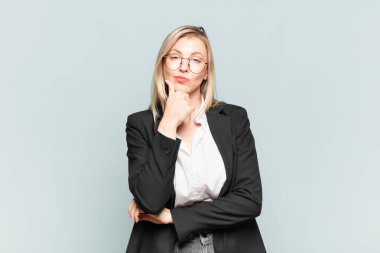 Genç ve güzel bir iş kadını ciddi, düşünceli ve güvensiz görünüyor, bir kolu çapraz ve çenesi üzerinde, seçenekleri tartıyor.