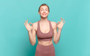 Genç sarışın kadın konsantre olmuş ve meditasyon yapıyor, kendini tatmin olmuş ve rahatlamış hissediyor, düşünüyor ya da bir seçim yapıyor. spor konsepti