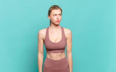 Genç sarışın kadın üzgün, üzgün ya da kızgın hissediyor ve olumsuz bir tavırla yan yana bakıyor, anlaşmazlık içinde kaşlarını çatıyor. spor konsepti