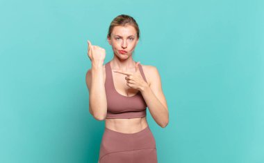 Genç sarışın kadın sabırsız ve kızgın görünüyor, saati gösteriyor, dakiklik istiyor, zamanında gelmek istiyor. spor konsepti