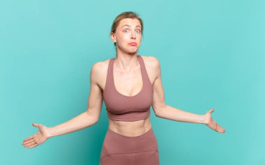 young blond woman feeling clueless and confused, having no idea, absolutely puzzled with a dumb or foolish look. sport concept