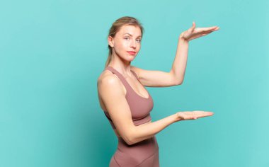 Genç sarışın bir kadın iki eli fotokopi alanında olan bir nesneyi tutuyor, bir nesneyi gösteriyor, sunuyor ya da reklamını yapıyor. spor konsepti