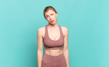 young blond woman feeling puzzled and confused, with a dumb, stunned expression looking at something unexpected. sport concept
