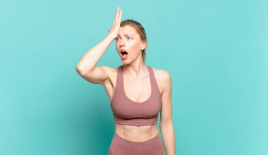 young blond woman raising palm to forehead thinking oops, after making a stupid mistake or remembering, feeling dumb. sport concept