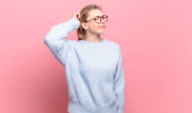 Genç, güzel sarışın kadın şaşkın ve kafası karışmış hissediyor, başını kaşıyor ve yan tarafa bakıyor.