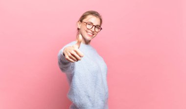 Genç, güzel sarışın kadın gururlu, tasasız, kendinden emin ve mutlu başparmaklarıyla gülümsüyor.