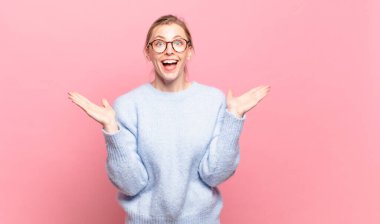 Genç, güzel sarışın kadın mutlu, heyecanlı, şaşırmış ya da şok olmuş hissediyor, gülümsüyor ve hayrete düşüyor.