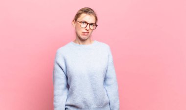 young pretty blond woman feeling puzzled and confused, with a dumb, stunned expression looking at something unexpected