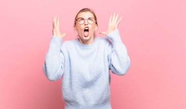 Genç, güzel sarışın kadın ellerini havaya kaldırarak bağırıyor. Öfkeli, sinirli, stresli ve üzgün.