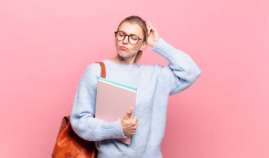 Genç, güzel bir öğrenci kafası karışmış ve kafası karışmış hissediyor, başını kaşıyor ve yan tarafa bakıyor.