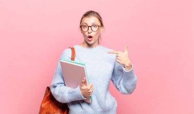Genç ve güzel bir öğrenci mutlu, şaşırmış ve gururlu. Heyecanlı ve şaşkın bir bakışla kendini işaret ediyor.