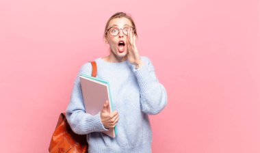 Genç, güzel bir öğrenci mutlu, heyecanlı ve pozitif hissediyor. Elleri ağızda, bağırarak bağırıyor.