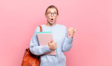 Genç ve güzel bir öğrenci inançsızlıktan şaşkın şaşkın bakıyor, yan taraftaki objeyi işaret ediyor ve 