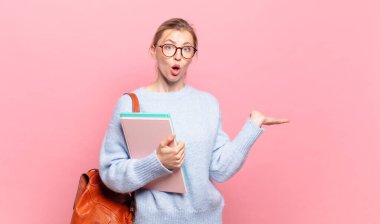 Genç ve güzel bir öğrenci şaşırmış ve şoka uğramış görünüyor, çenesi düşmüş, bir objeyi elinde açık bir elle tutuyor.