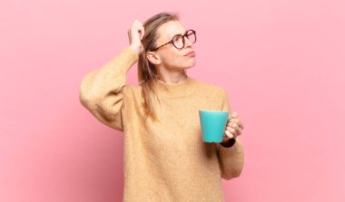 Genç sarışın kadın şaşkın ve şaşkın hissediyor, başını kaşıyor ve yana bakıyor. kahve konsepti