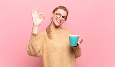 Genç sarışın kadın kendini mutlu, rahat ve tatmin olmuş hissediyor. Güzel bir jestle onaylıyor, gülümsüyor. kahve konsepti