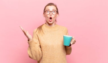 Genç sarışın kadın ağzı açık ve şaşkın, şok olmuş ve hayrete düşmüş inanılmaz bir sürprizle. kahve konsepti