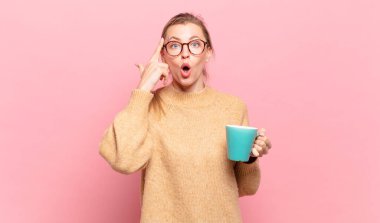 Genç sarışın kadın şaşırmış, ağzı açık, şok olmuş, yeni bir düşünce, fikir ya da konsept keşfediyor. kahve konsepti