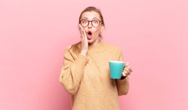 Genç sarışın kadın şok olmuş ve korkmuş hissediyor, ağzı açık ve elleri yanaklarında korkmuş görünüyor. kahve konsepti