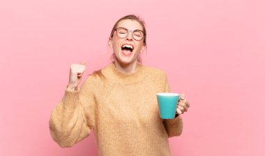 Genç sarışın kadın kızgın bir ifadeyle agresif bir şekilde bağırıyor ya da yumruklarıyla başarıyı kutluyor. kahve konsepti