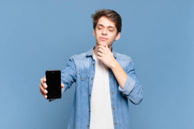 Genç bir çocuk mutlu, kendinden emin bir ifadeyle gülümsüyor, çenesi elleri çenesinde, merak ediyor ve yana bakıyor. telefon kavramı