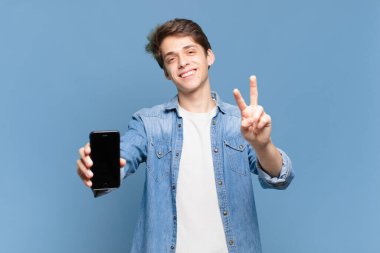 Genç bir çocuk gülümsüyor ve mutlu görünüyor, tasasız ve olumlu, bir eliyle zafer ya da barışı simgeliyor. telefon kavramı