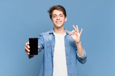 Genç çocuk kendini mutlu, rahat ve tatmin olmuş hissediyor. İyi bir jestle onaylıyor, gülümsüyor. telefon kavramı
