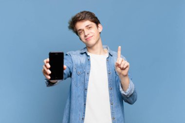 Genç bir çocuk gülümsüyor ve arkadaş canlısı görünüyor, bir numarayı gösteriyor ya da ilk eli önde, geri sayıyor. telefon kavramı