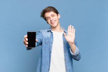 Genç çocuk mutlu ve neşeyle gülümsüyor, el sallıyor, seni selamlıyor ve selamlıyor, ya da hoşça kal diyor. telefon kavramı