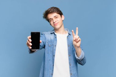 Genç bir çocuk gülümsüyor ve arkadaş canlısı görünüyor. İki ya da iki numarayı gösteriyor. Elleri önde, geriye doğru sayıyor. telefon kavramı