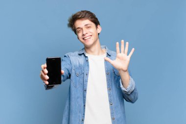 Genç bir çocuk gülümsüyor ve dost canlısı görünüyor. Beş ya da beş numarayı gösteriyor. Elleri önde, geriye doğru sayıyor. telefon kavramı