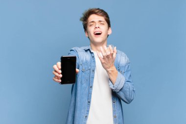 Genç çocuk umutsuz ve sinirli görünüyor, stresli, mutsuz ve sinirli, bağırıyor ve çığlık atıyor. telefon kavramı