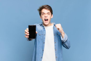 Genç bir çocuk öfkeli bir ifadeyle ya da yumruklarıyla başarıyı kutlarken agresif bir şekilde bağırıyor. telefon kavramı